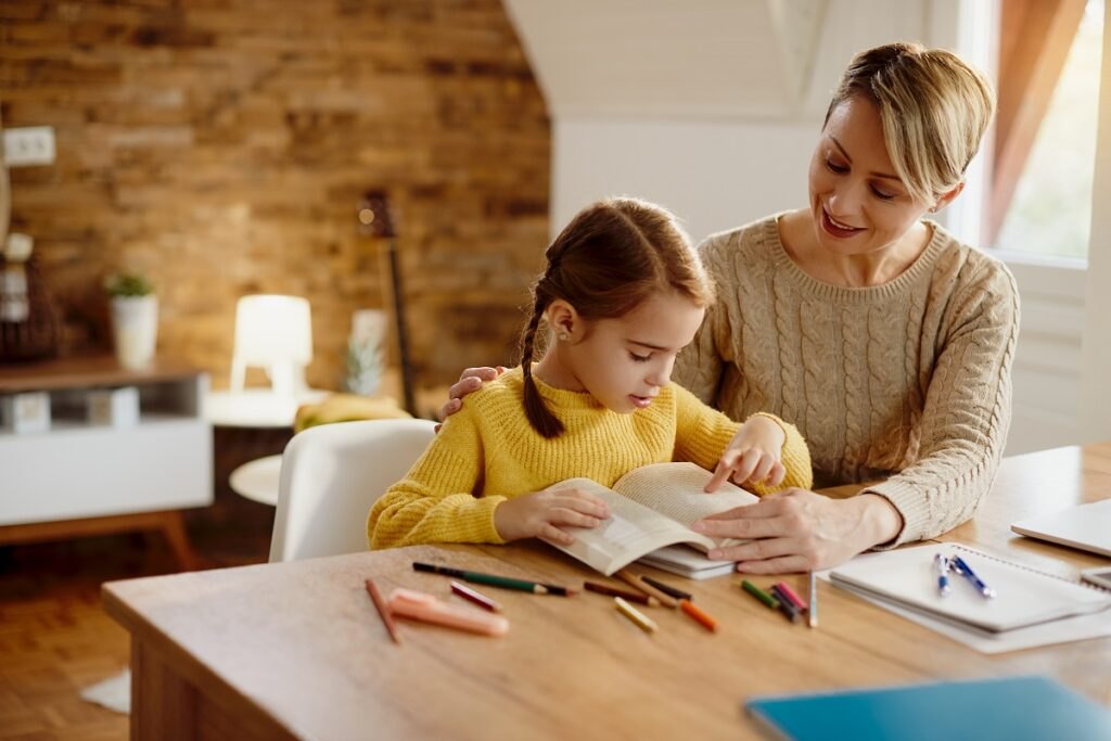 Jak zachęcić dziecko do nauki? Small-girl-reading-book-while-learning-with-help-her-mother-home