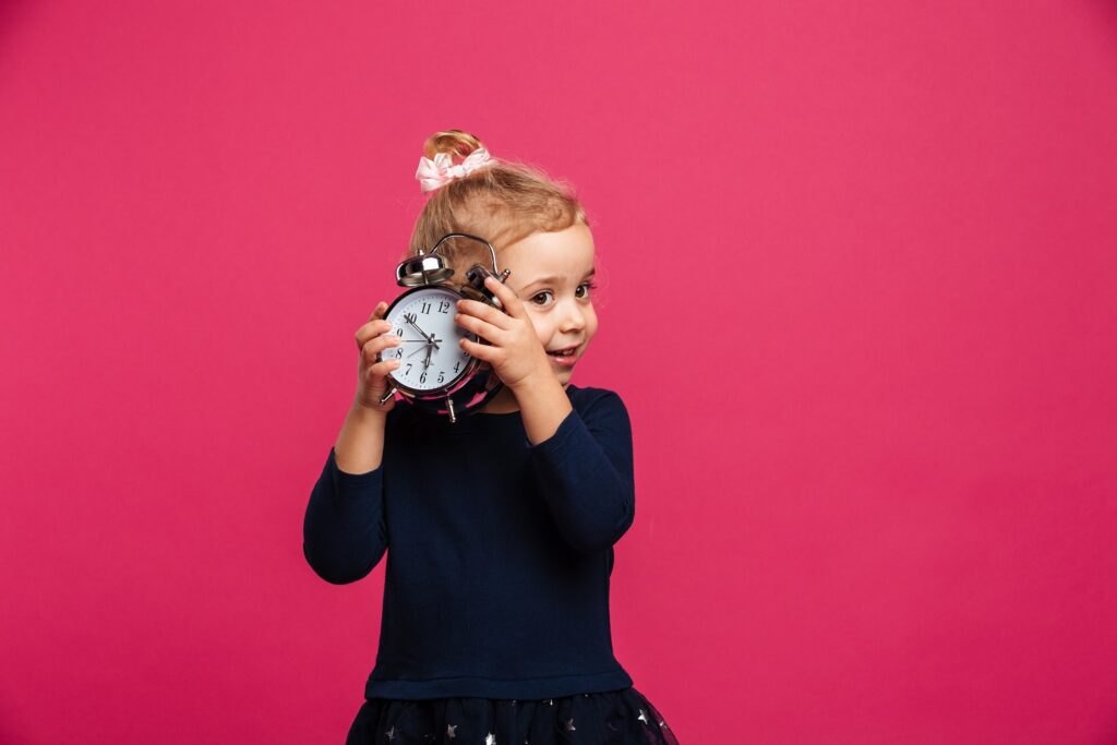 Nauka zegara dla dzieci: pomocne wskazówki Intrigued-young-blonde-girl-holding-alarm-clock-pink-wall